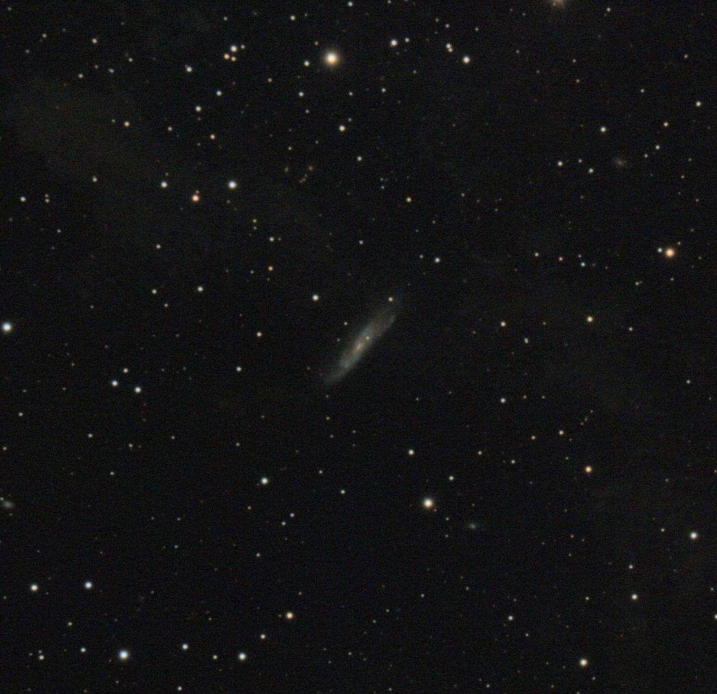 A spiral galaxy with a hint of white colored nebulosity in the background.