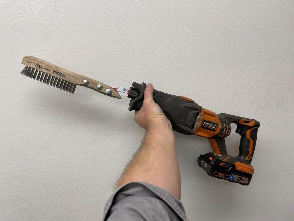 Someone has taken the time to connect a reciprocating saw's blade to a wire brush handle, allowing a battery operated reciprocating saw to act as a high-speed wire brush for back-and-forth brushing.