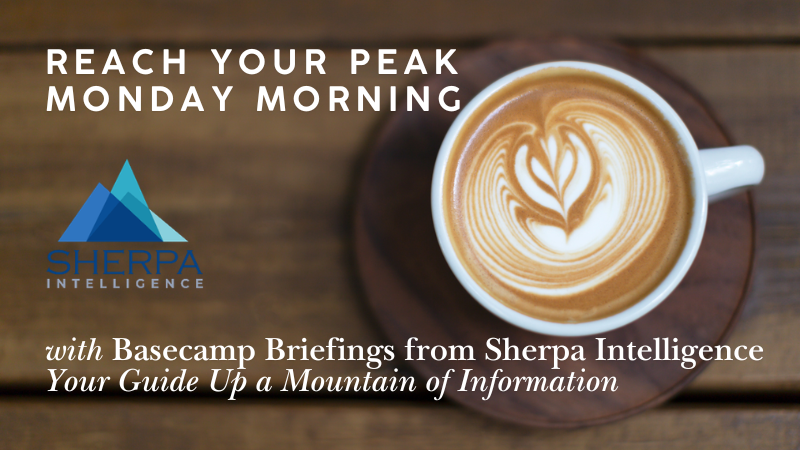 A promotional graphic with a wooden table background. On the right is a white mug filled with coffee featuring leaf-patterned latte art on a wooden saucer. On the left, bold white text reads "REACH YOUR PEAK MONDAY MORNING" above the Sherpa Intelligence logo, which consists of three overlapping blue and teal mountain peaks. At the bottom, white italicized text reads "with Basecamp Briefings from Sherpa Intelligence. Your Guide Up a Mountain of Information."
