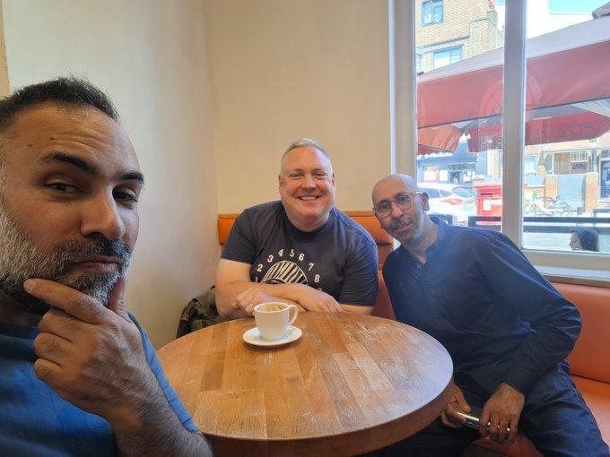 Javvad, Dan, and Mo, sitting in a cafe with one cup of coffee on the table.