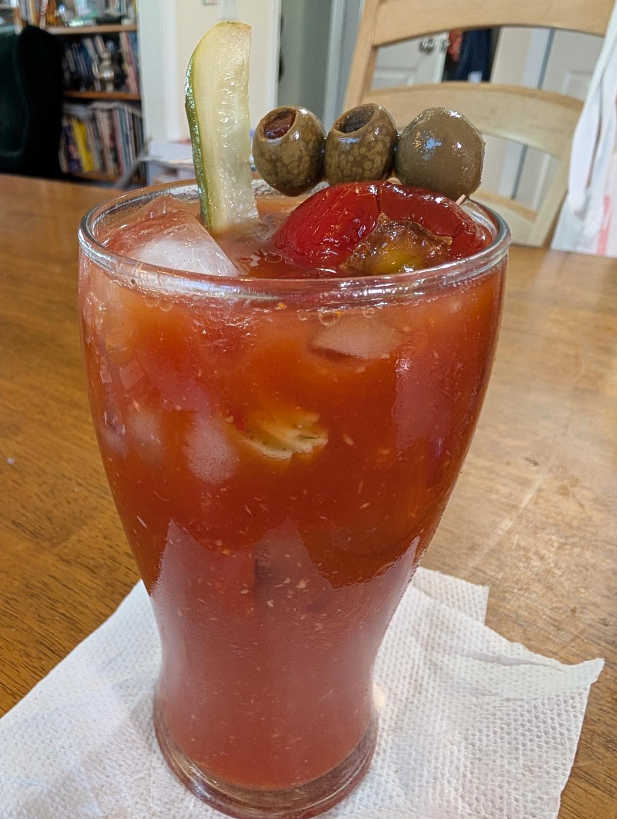 A tall glass with a bloody Mary garnished with olives, a pickled cherry pepper and a pickle.
