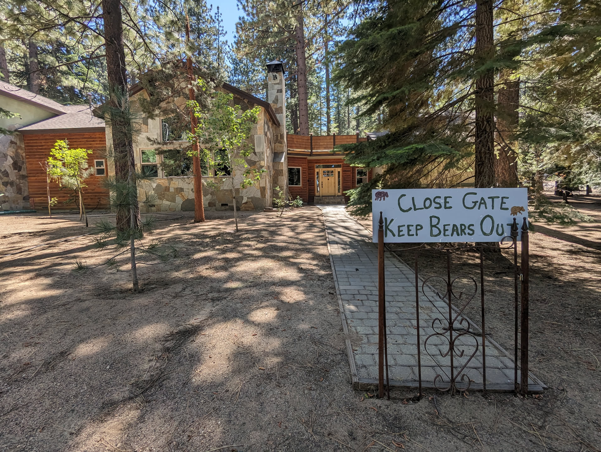 An open front yard with a solitary gate at the end of a sidewalk.  On the gate is a hand-written sign that reads "Close Gate.  Keep Bears Out."