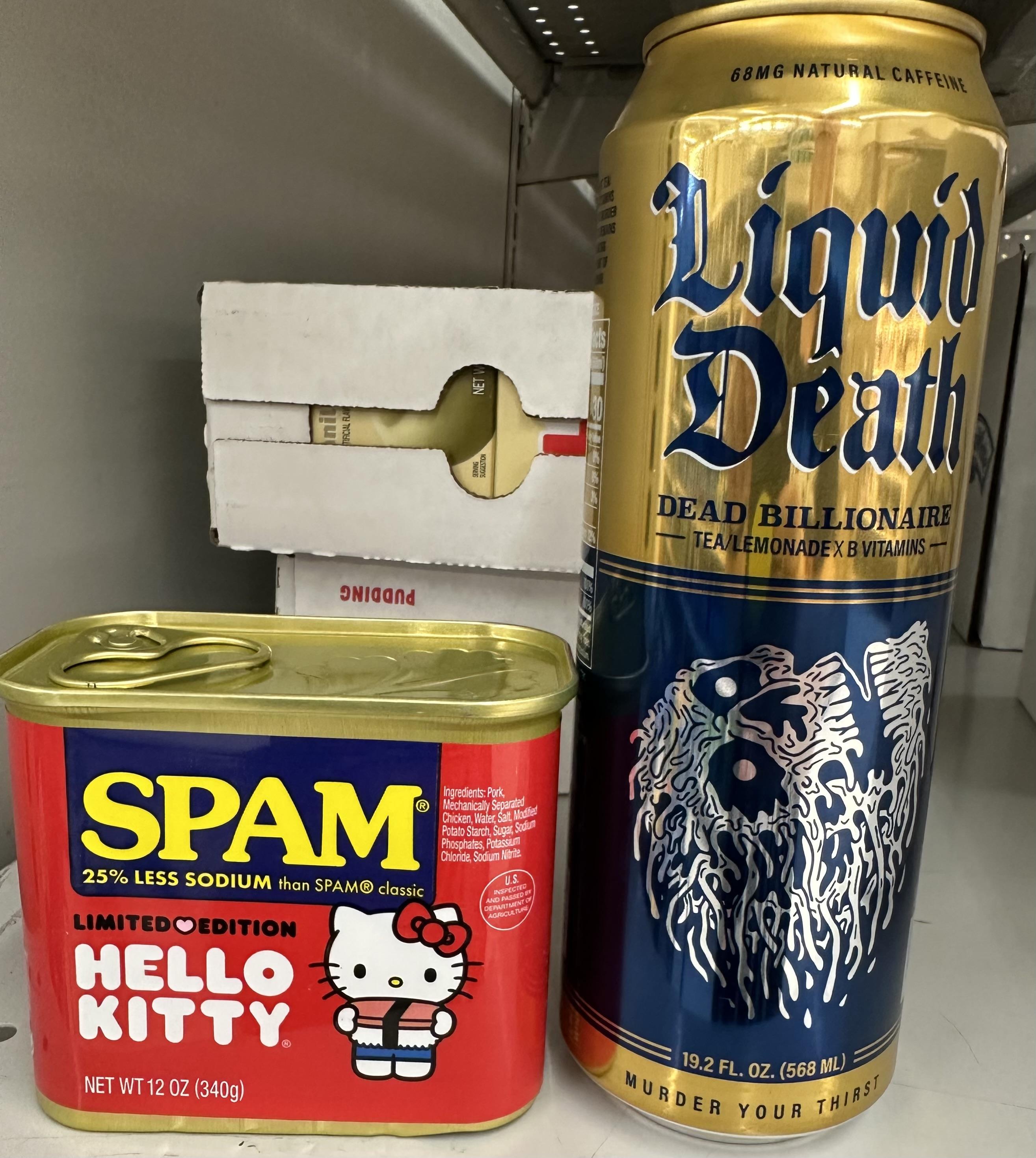 A photo of two cans staged on a grocery store shelf. One can has a red label and is the "Hello Kitty" limited edition can of lower sodium SPAM showing Hello Kitty holding a large SPAM musubi; the second can is Liquid Death brand iced tea/lemonade mix, with a flavor name of "Dead Billionaire". The SPAM presumably tastes like salty pork, the Liquid Death fortunately does not taste of dead billionaire (and unfortunately also not much of tea or lemonade).