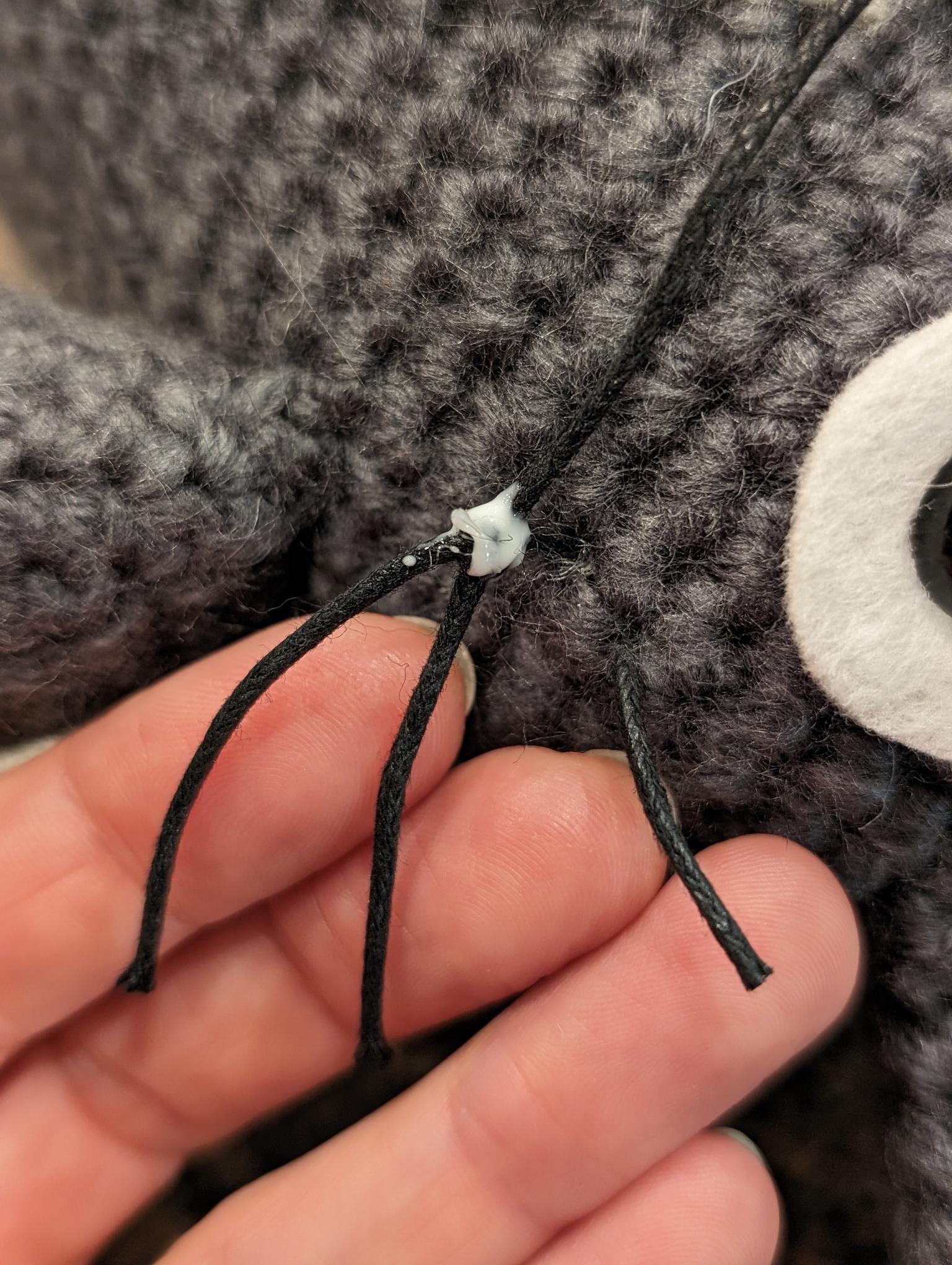 close-up of waxed-cotton-cord whiskers - I needed groups of three, so I cut one length 2x, tied a third in the middle, put a dot of glue to keep the knot from coming undone, and then sunk the knot and pulled each of the three whiskers out between different stitches.  there's probably a better / easier way, but it worked!
