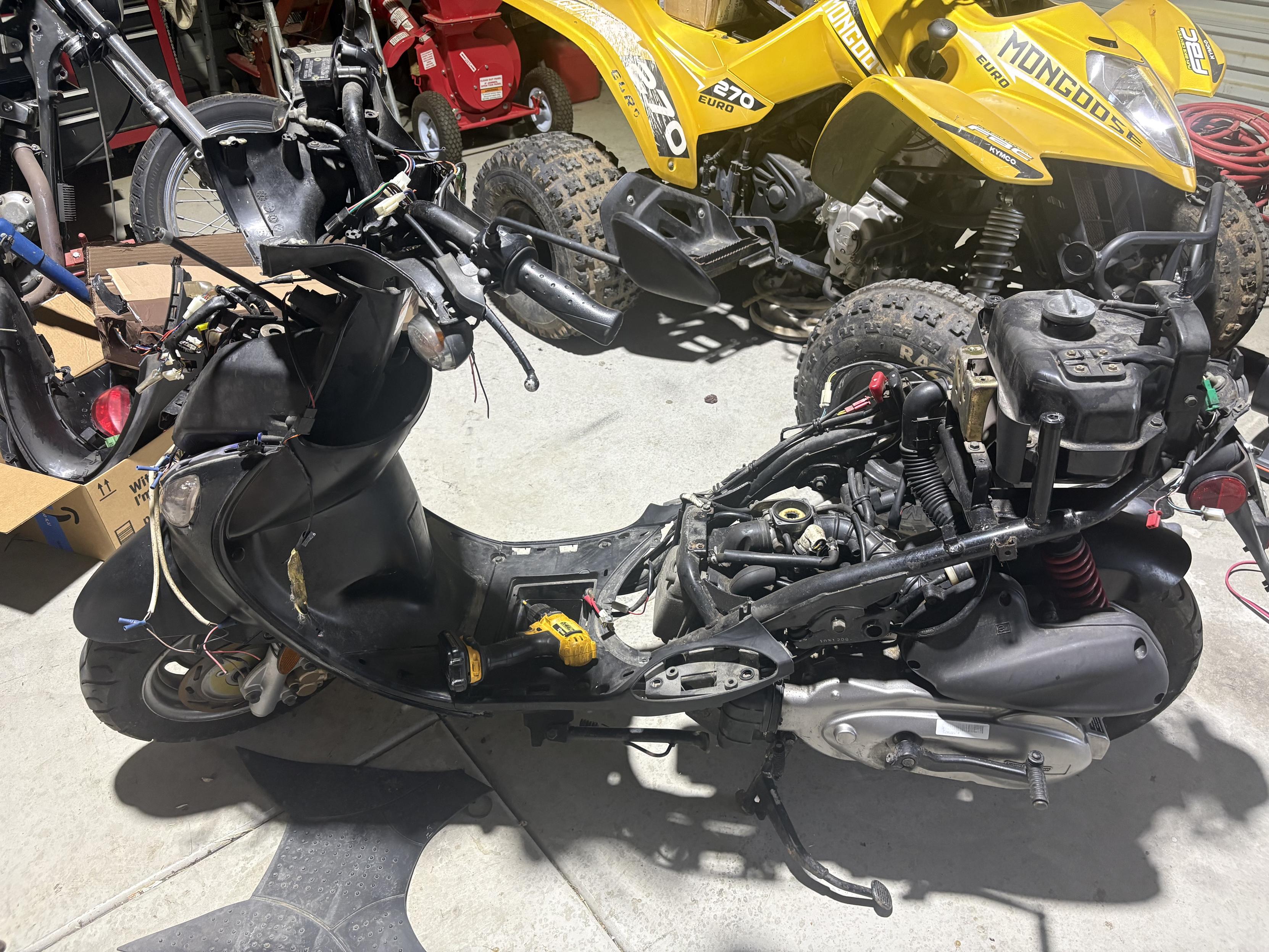A motor scooter with most of the plastic fairing removed and some witing guts hanging out the front.