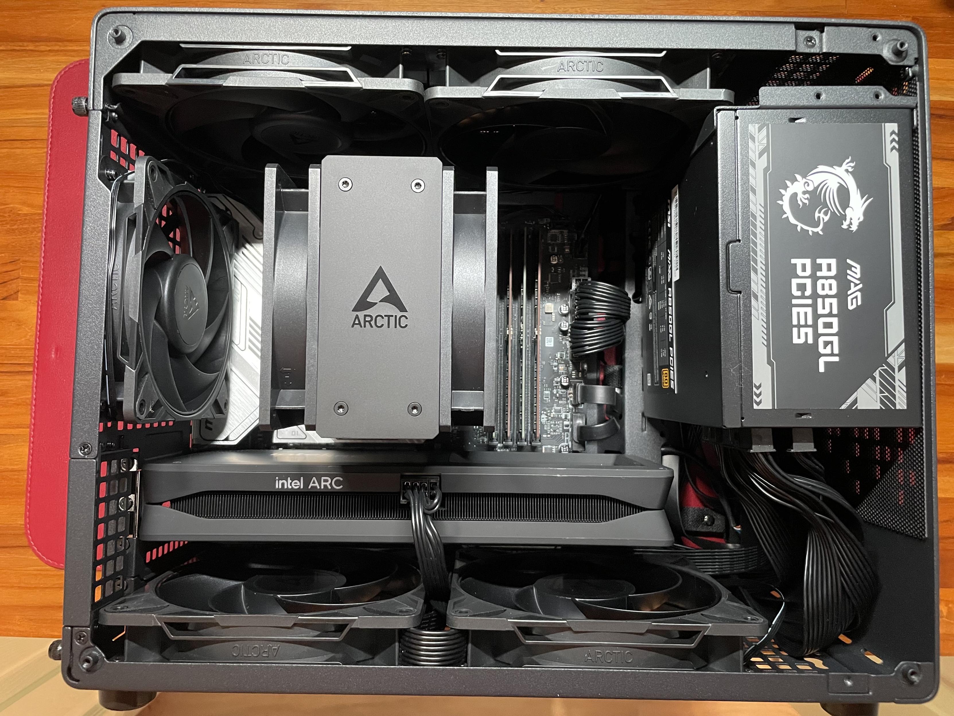 The inside of my new mATX computer build. There are numerous fans, the COU cooler dominating the center of the case with a large Arctic logo. The PSU sits to the right of the case, and the Intel Arc GPU sits below.