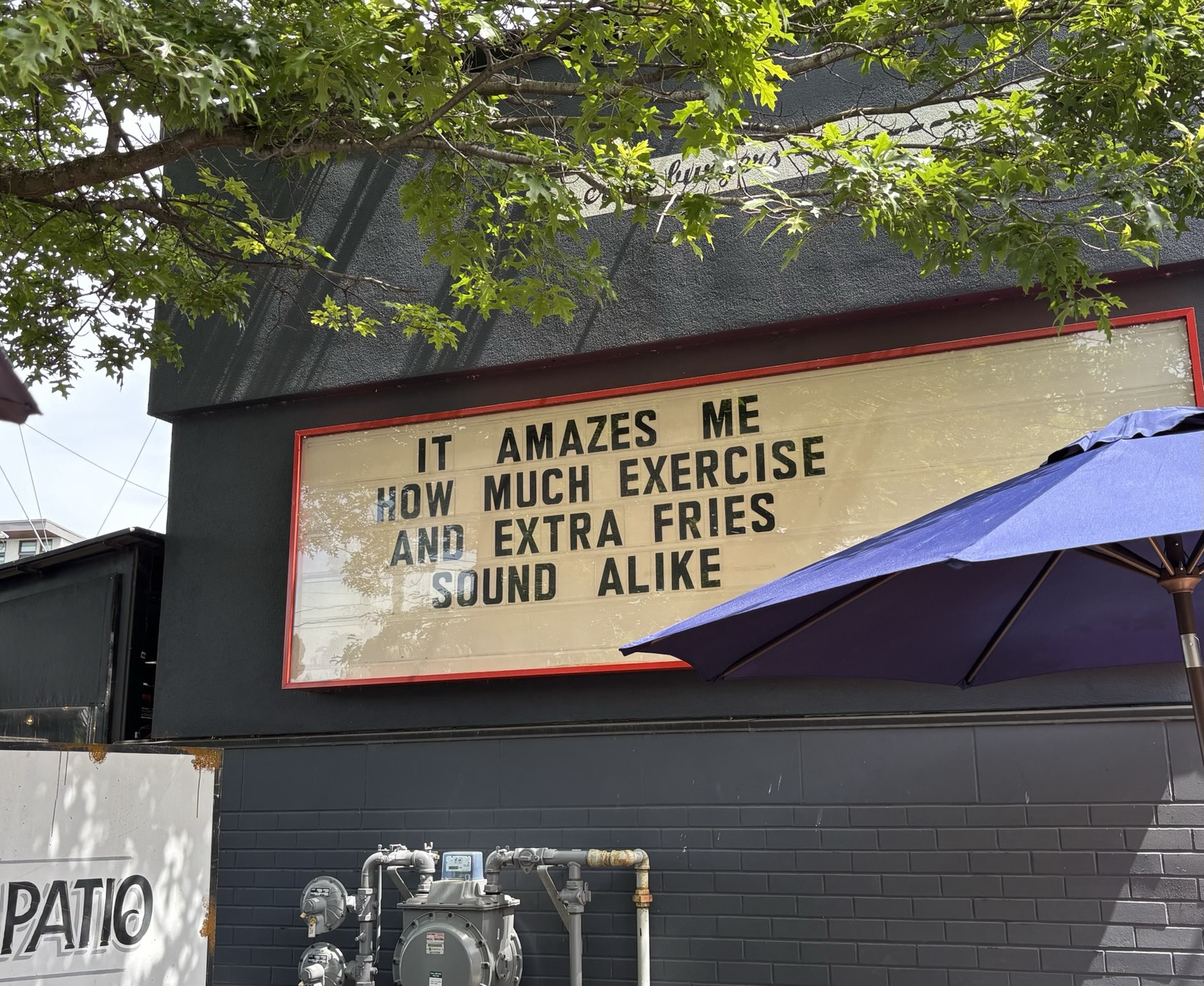 A sign on the side of a building. Text: “It amazes me how much exercise and extra fries sound alike”