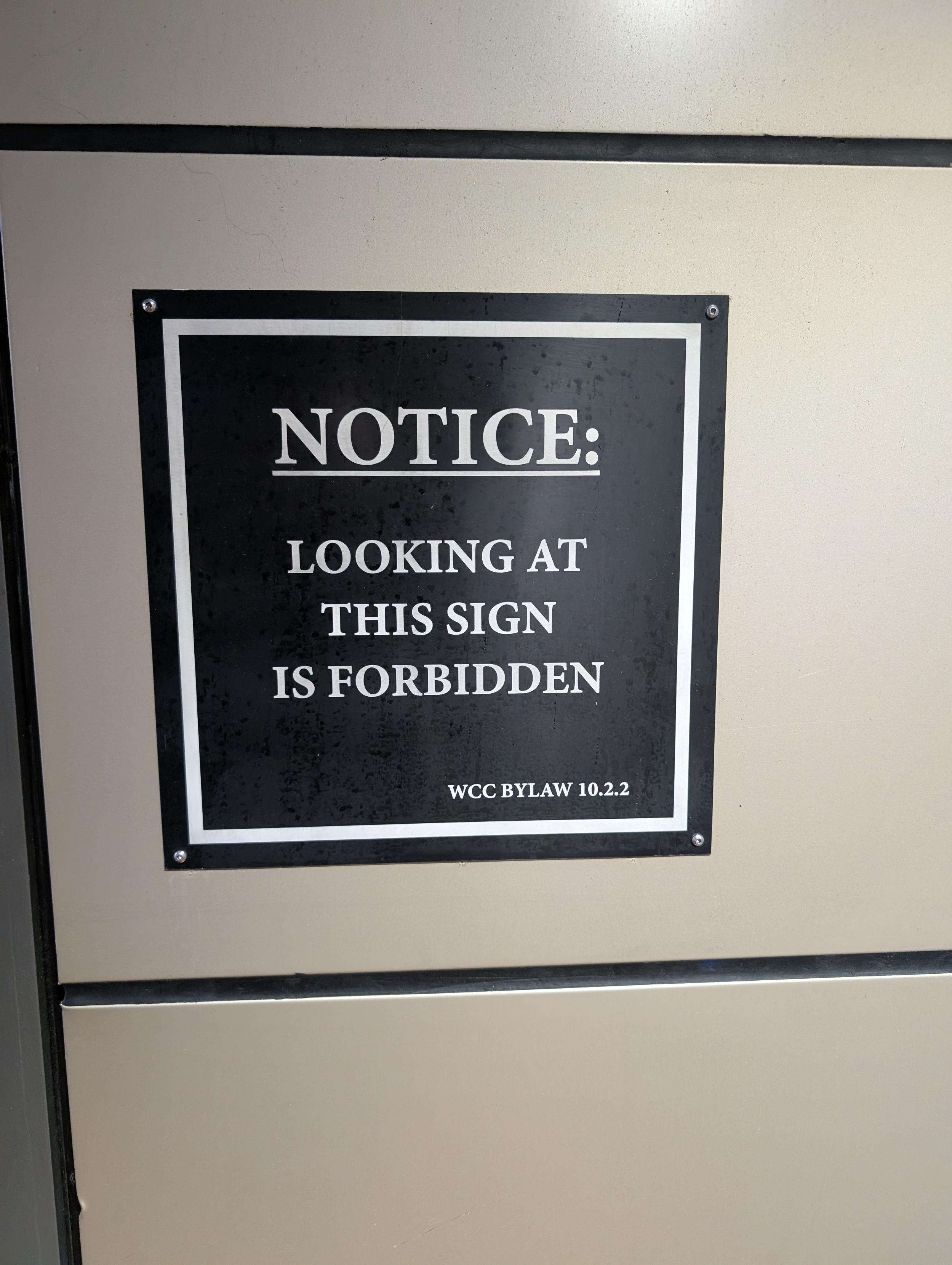 A sign on a wall which says “notice: looking at this sign is forbidden wcc bylaw 10.2.2”
