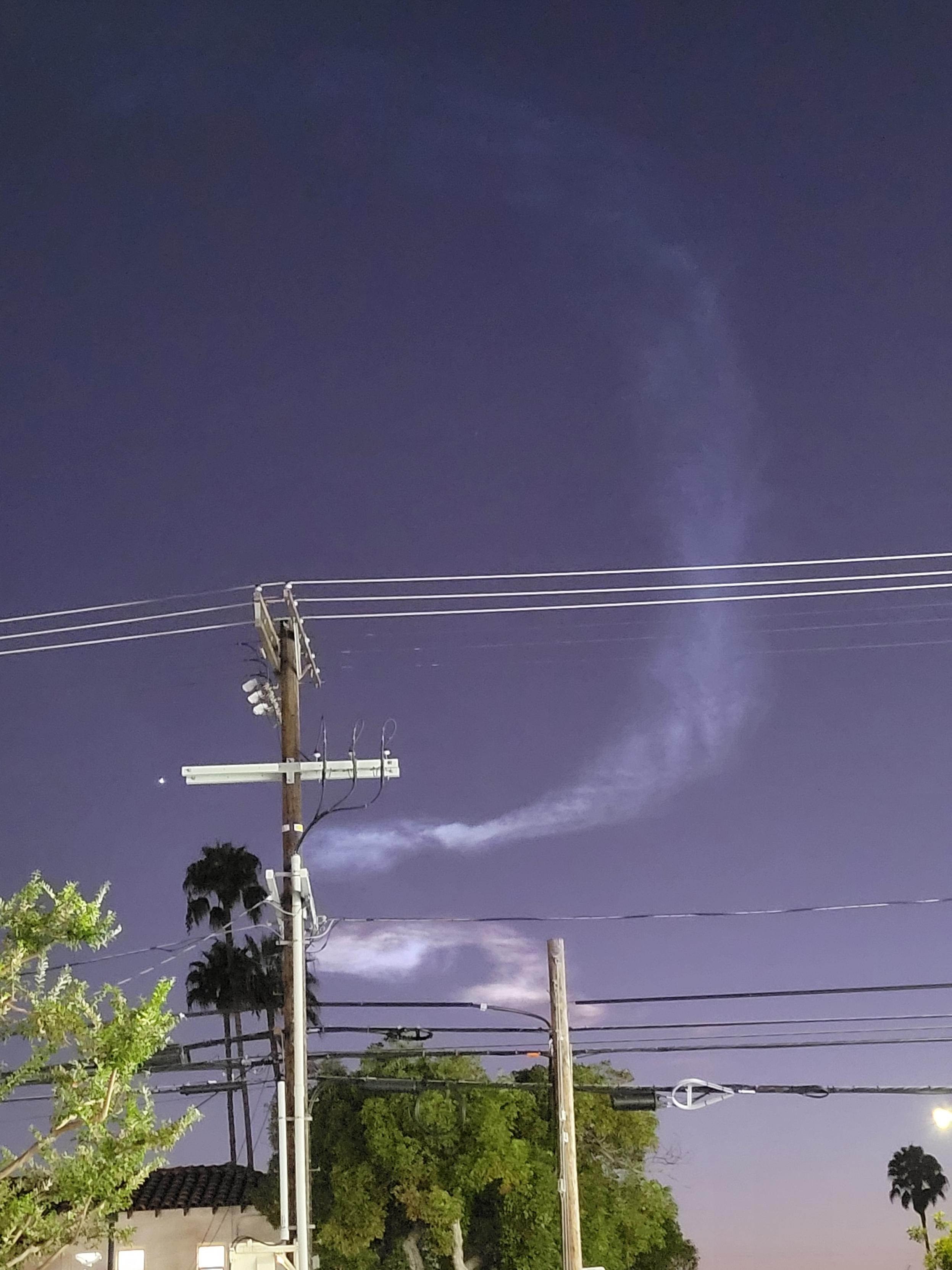 Blown-out photo of two clouds behind power lines and palm trees in an otherwise nearly featureless purple evening sky. The clouds look like wide, swirling doodles, the top one blue and the bottom one pink. To the left of one utility pole is the lone visible star, which is probably actually the planet Venus. The picture is overly bright because it is lit by businesses on La Brea Ave.