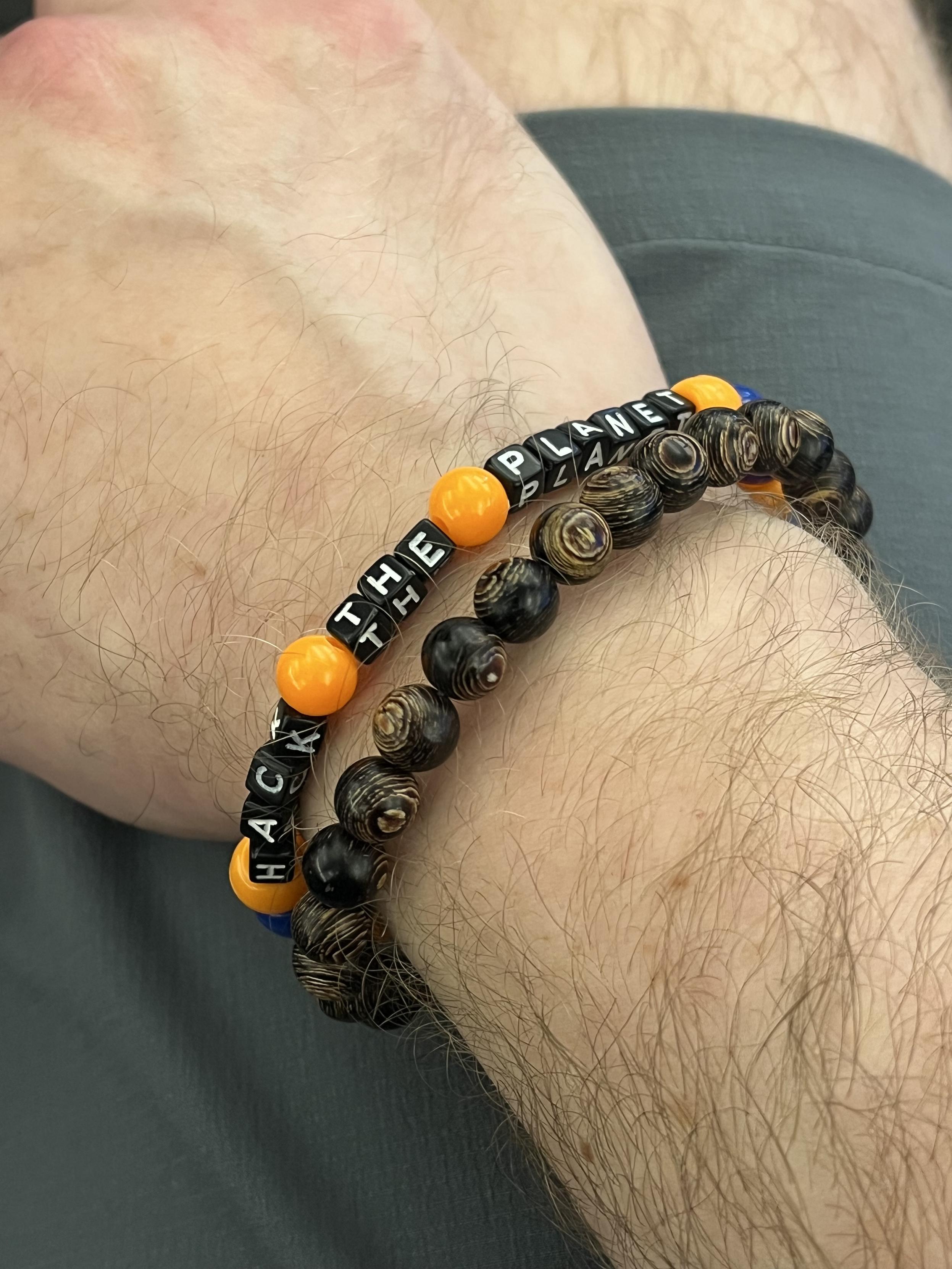 A picture of a man’s wrist wearing an Arcanum InfoSec friendship bracelet that reads “HACK THE PLANET”