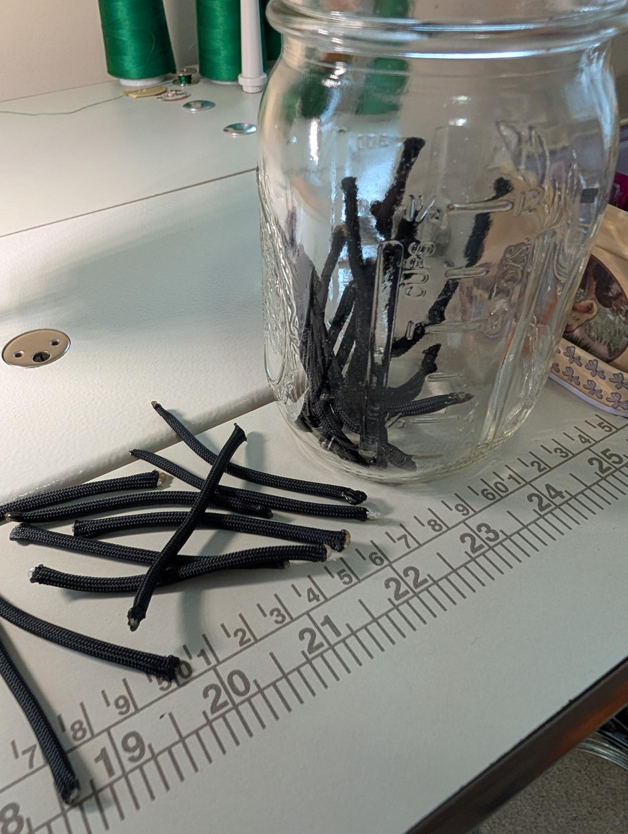 A mason jar with nylon cord lengths next to a modest pile of cord bits