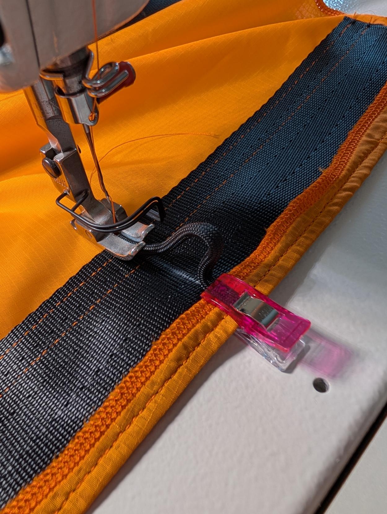 An industrial sewing machine set up to sew a length of nylon cord onto webbing