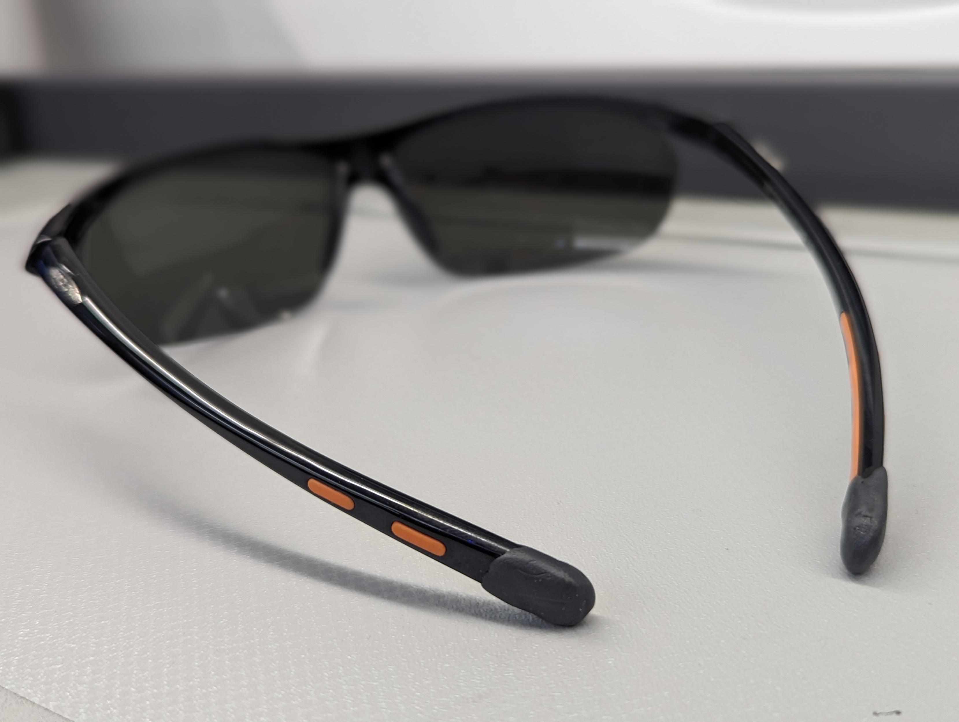Sport sunglasses on a nondescript beige counter. The tip of the temple (leg) is covered in a bespoke, hand-smoothed blob of black Sugru.