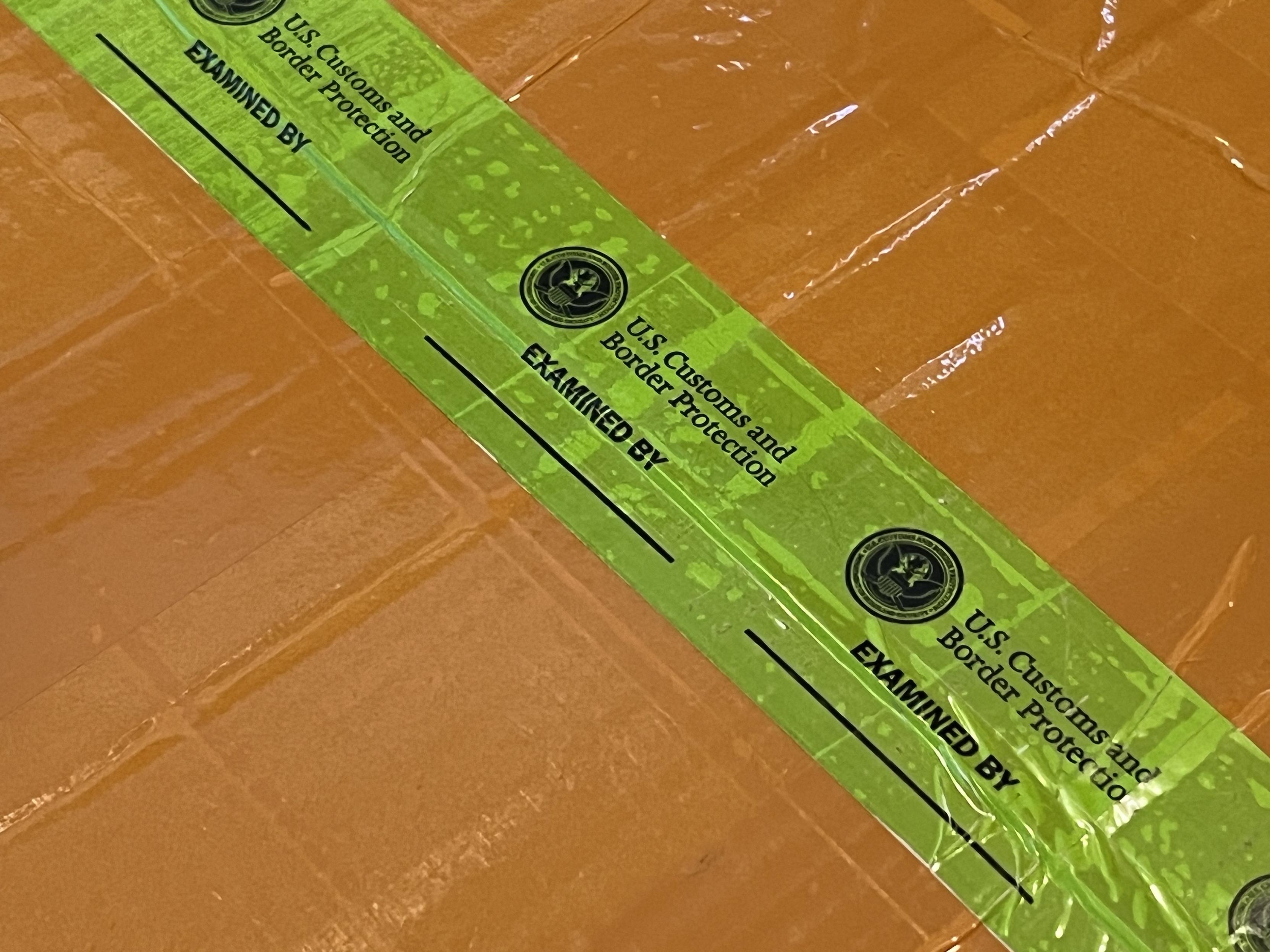 Close-up of the green tape, repeatedly reading:
 “U.S. Customs and
Border Protection 
EXAMINED BY
_____________”

Notably, none of the lines that are supposed to have a name/initial/number have anything written.