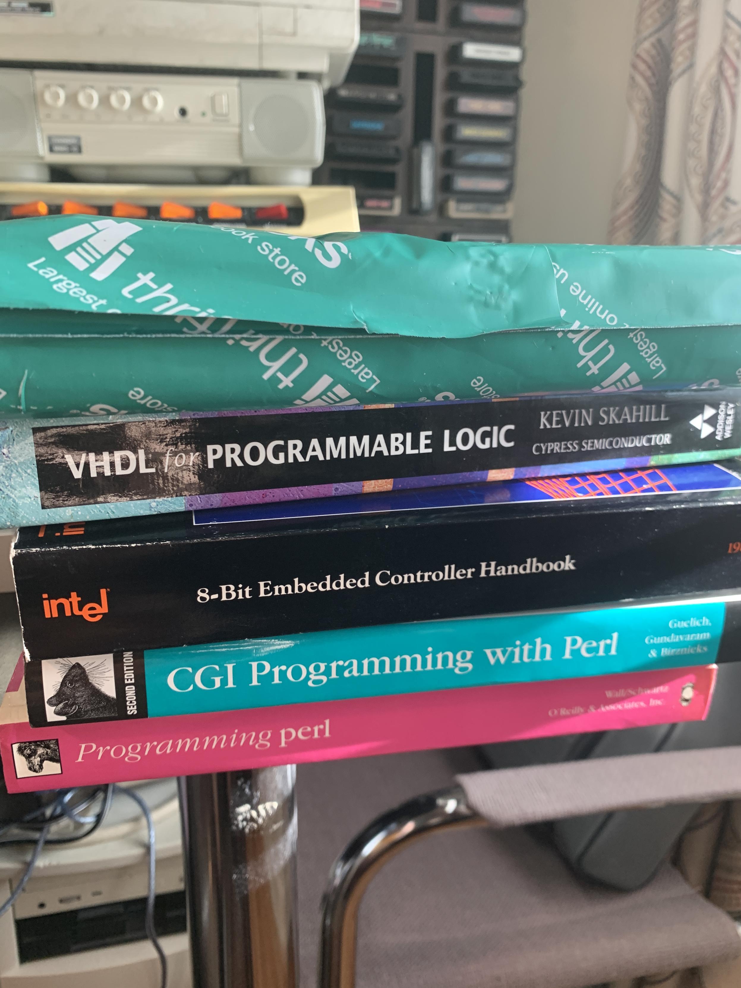 Stack of books on a black table: oreily programming Perl, oreily cgi programming with Perl, intel 8-bit embedded controller handbook, VHDL for programmable logic and a mystery book from thrift books on line