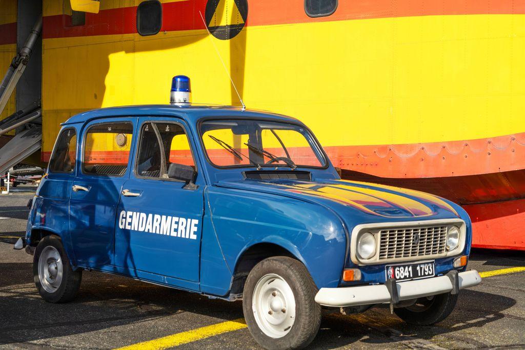 An ancient but well restored/cared for Renault police car in blue pictured against a bright yellow ship side.