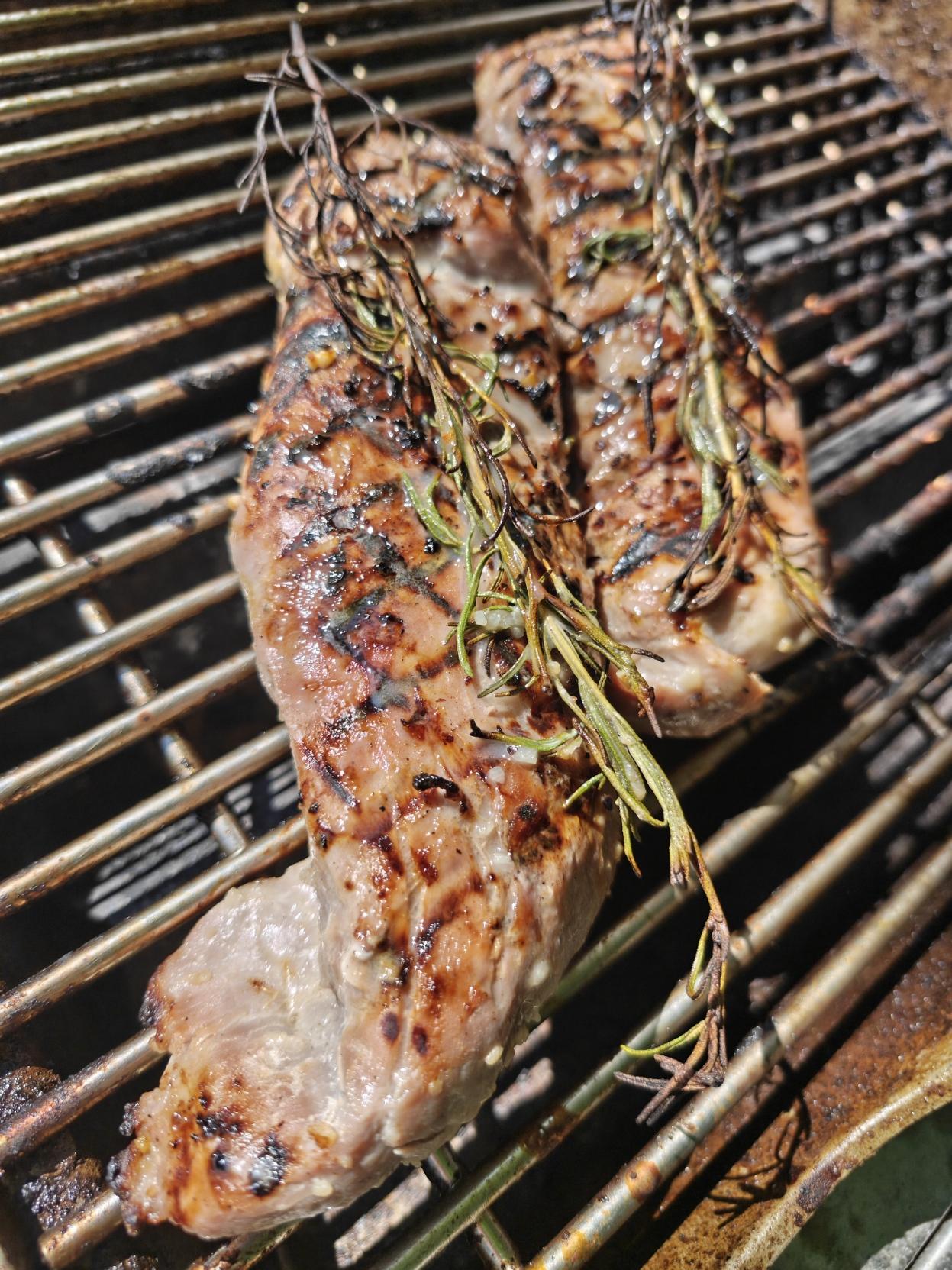 Two pork tenderloins with marinade and rosemary sitting on top like I'm some kind of fancy griller.
