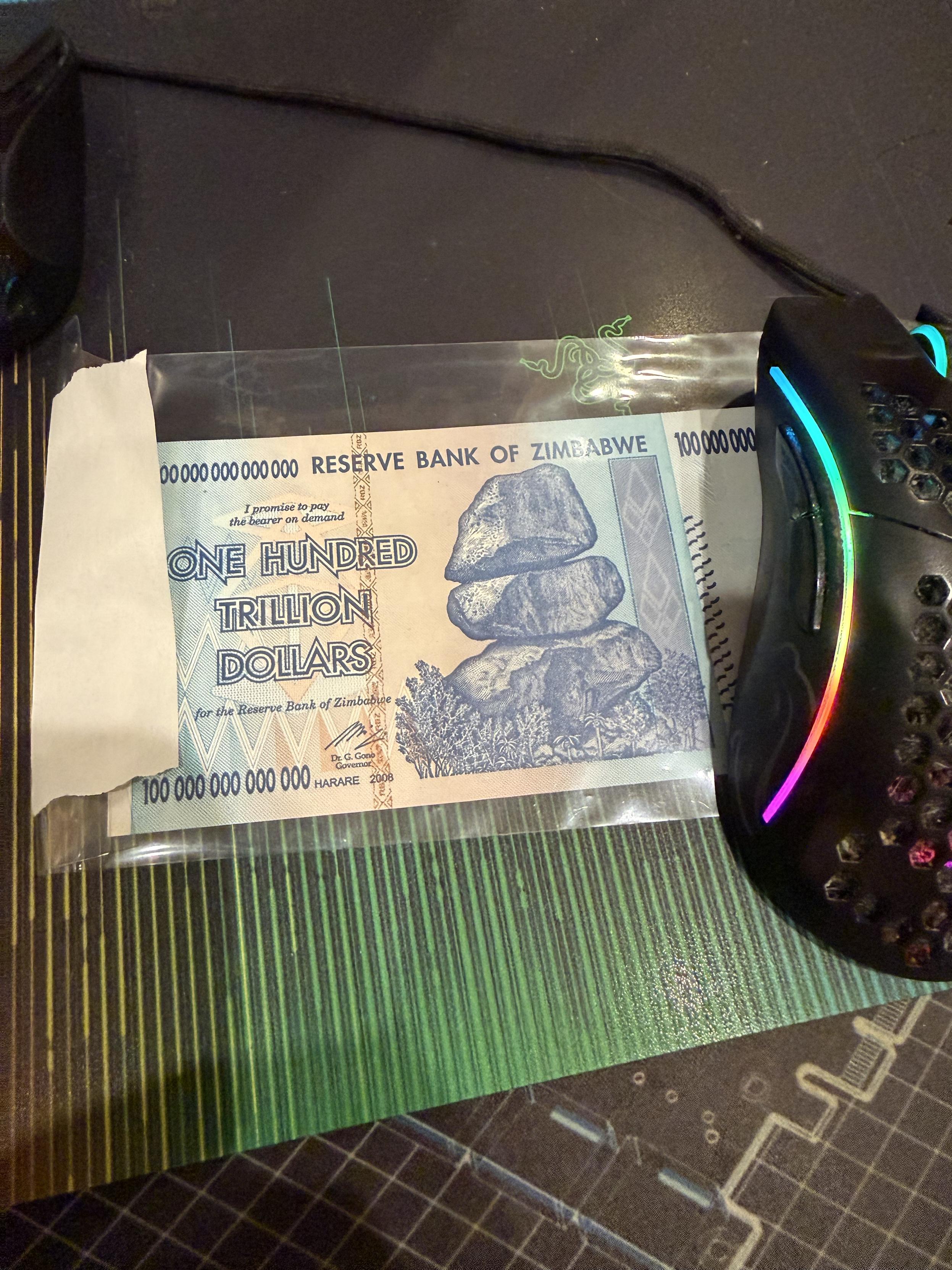 Reserve bank of Zimbabwe $100 trillion note on a mouse pad LED mouse on right