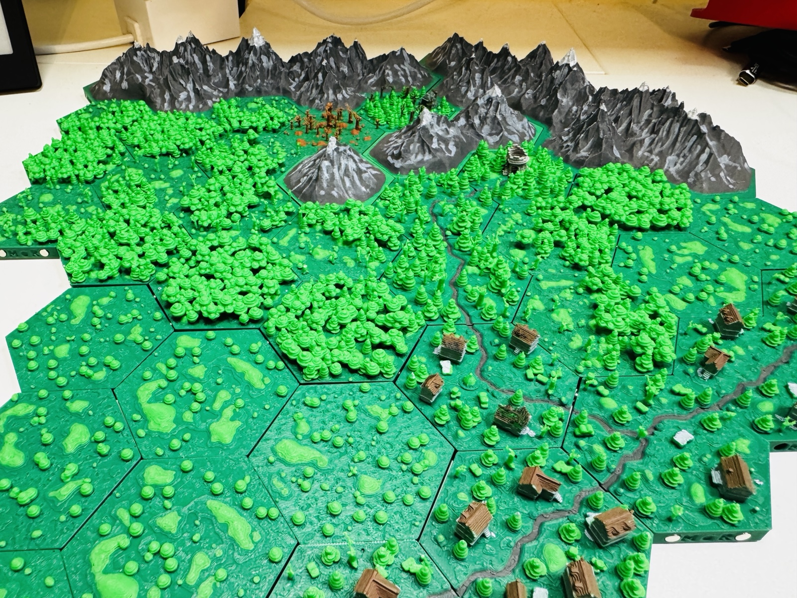 Fantasy 3D map for a TTRPG. The map is photographed from above. 

One can see that the scenario is built from hex tiles. In the map you see roads, buildings, forests, a ruined tower and mountains at the top.