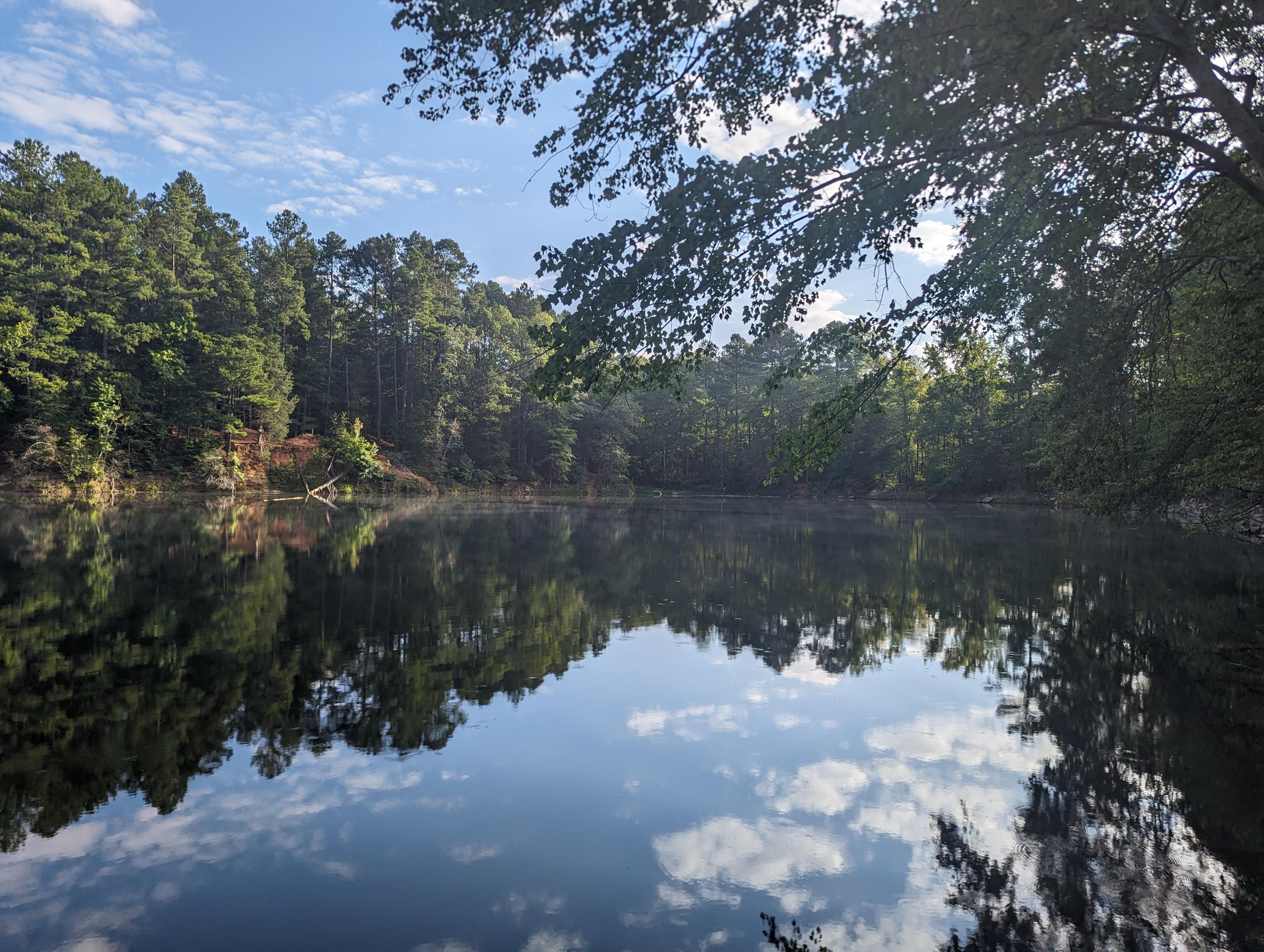 Trees, blue sky, and clouds reflecting in the still water of the (flooded) Eno Quarry.