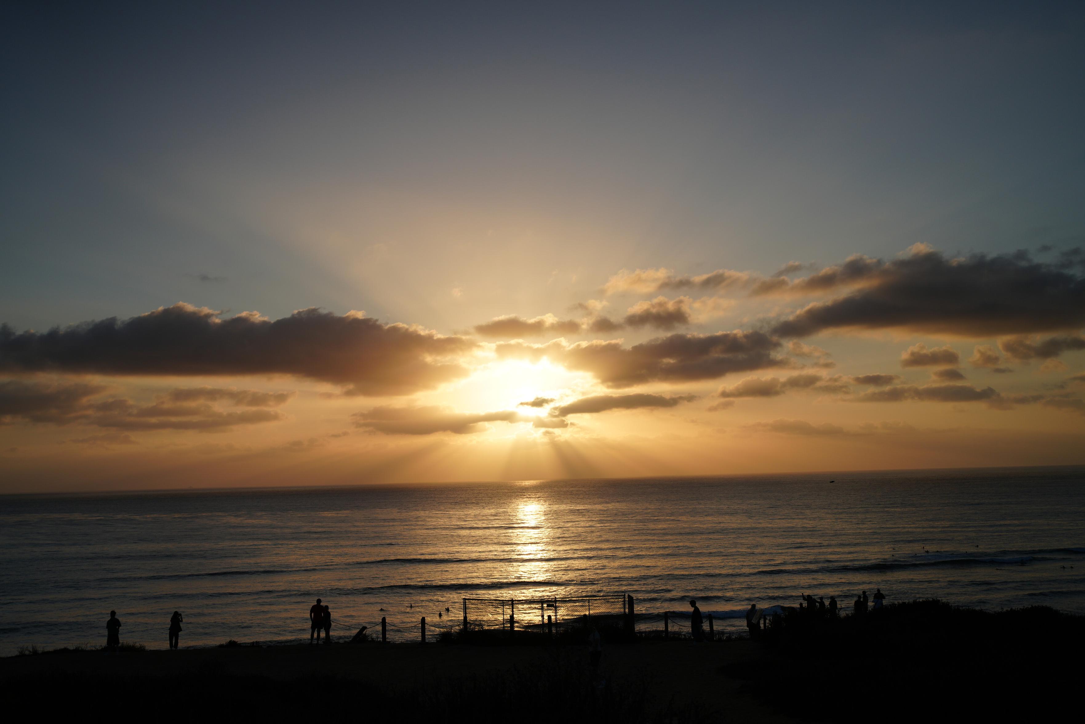 Photo of a sunset over a beach, pretty dark. A couple is standing close in the bottom left. Shot with Tamron 20-40mm f2.8