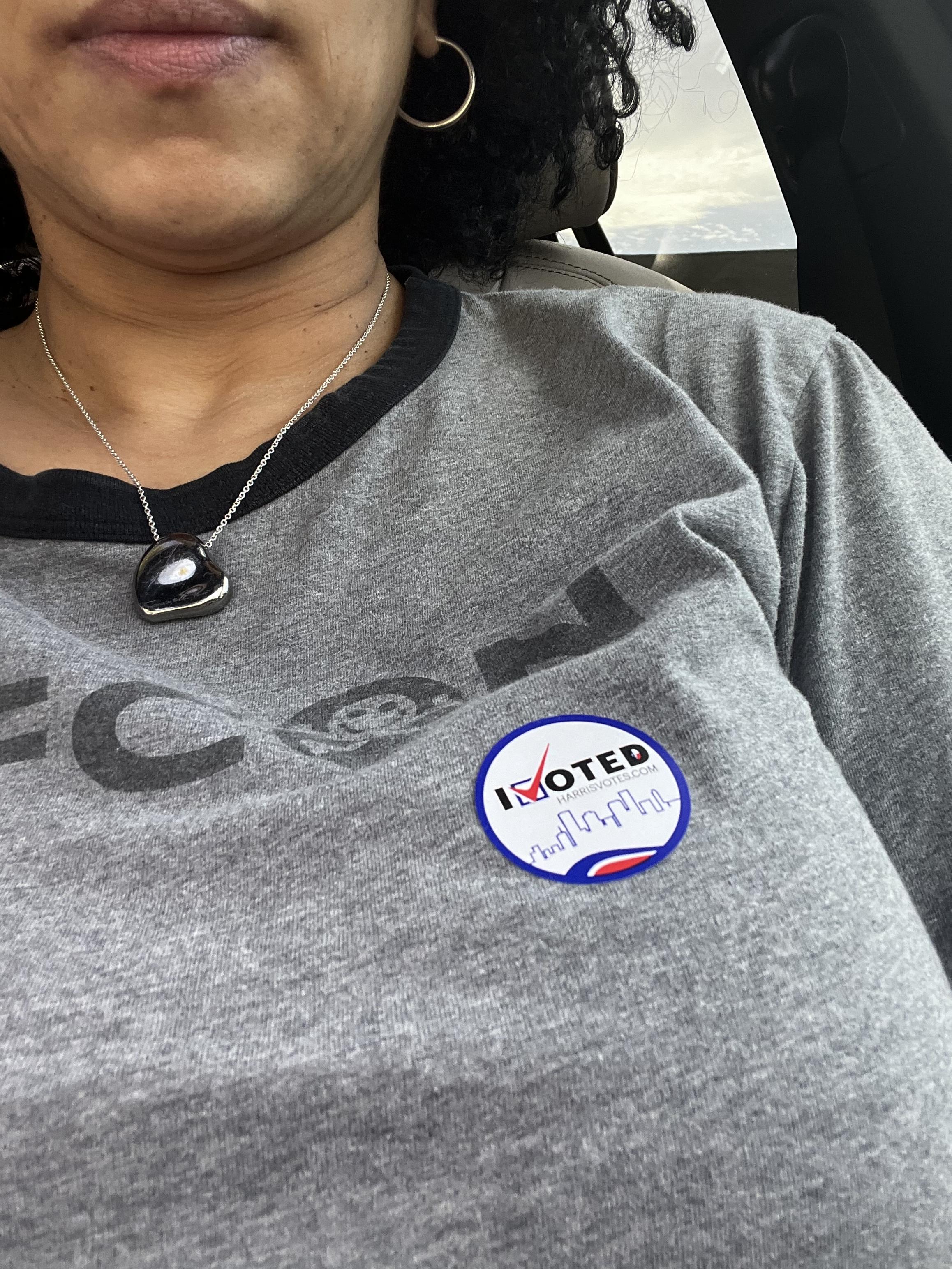 A person wearing a gray shirt with a "I VOTED" sticker on the chest.