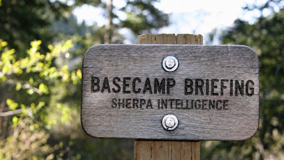Alt-Text for Image: Split-pane promotional graphic. The top solid-color panel details the Sherpa Intelligence Basecamp Briefing for October 19, 2026, including a Substack URL. The bottom panel displays a photo of a wooden forest trail sign mirroring the same title and branding.