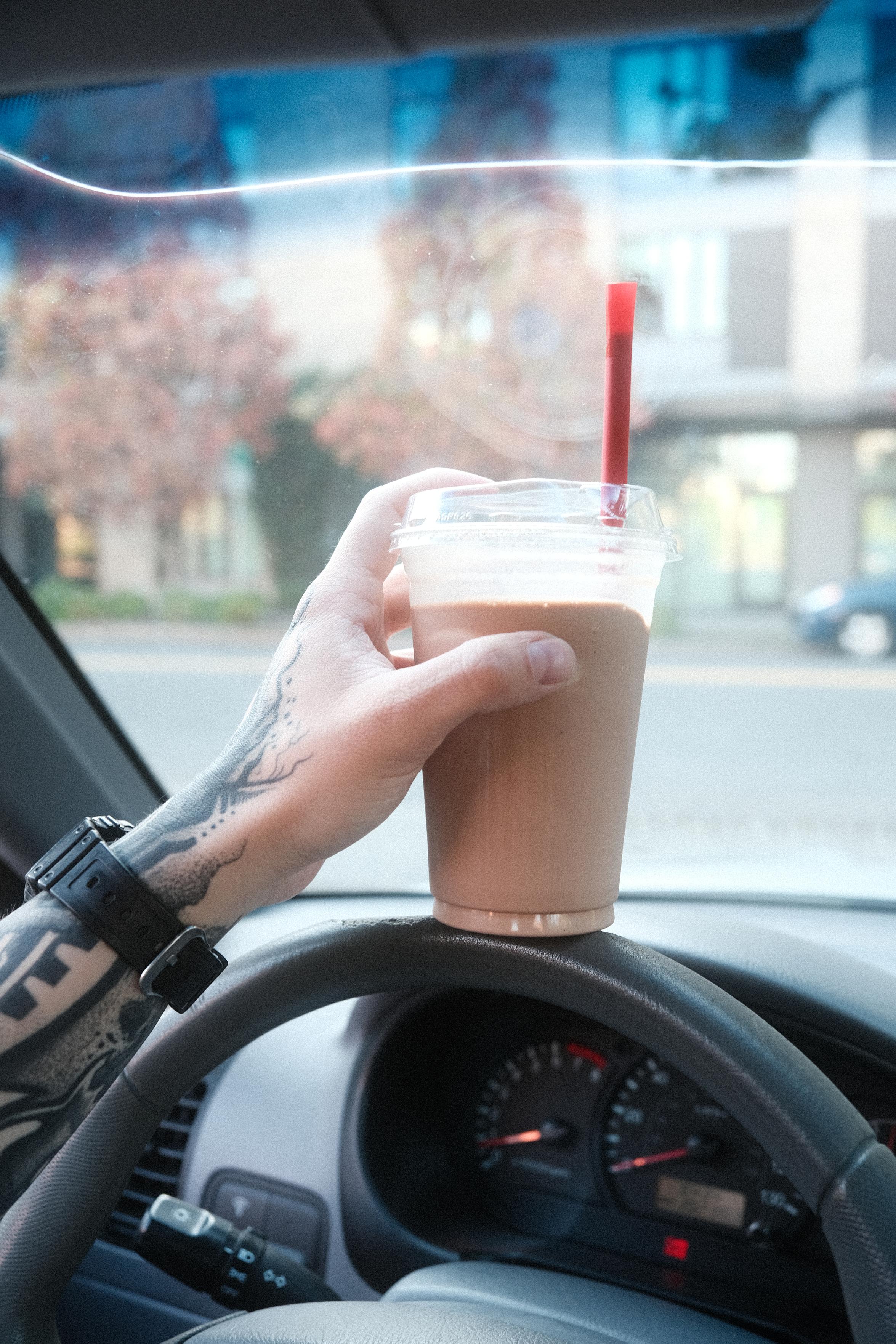 raven holding a milkshake while parked in a car