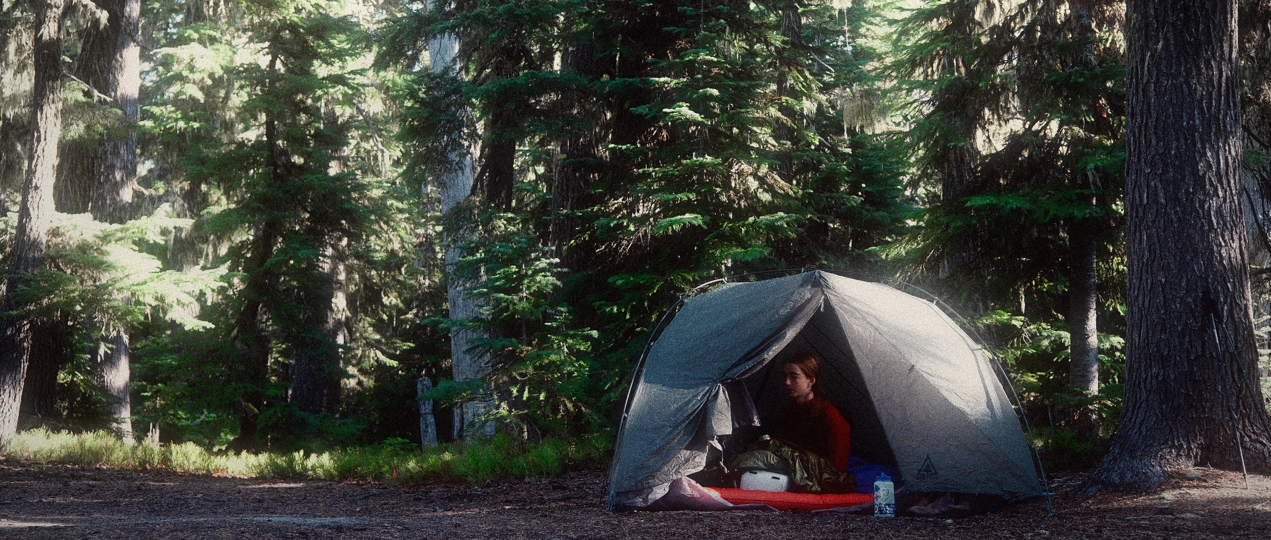 a tent in a forest with the rainfly slightly ajar to reveal natalie sitting in the tent trying to get warm