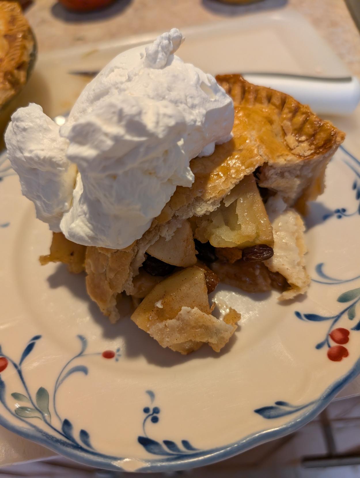 A slice of apple pie with a large dollop of whipped cream on top.