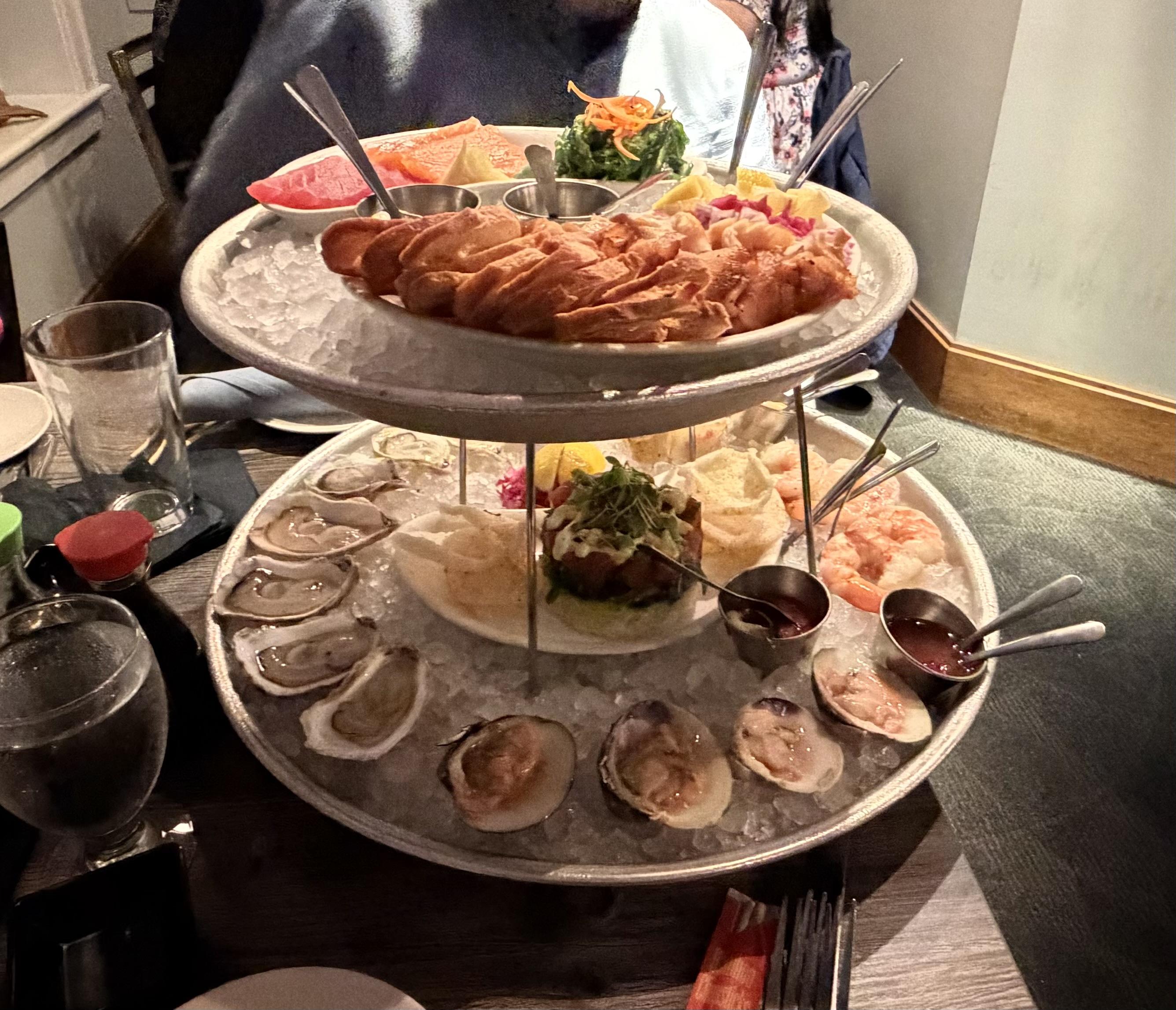 Photo if a two tier seafood tower with shellfish and sashimi on it