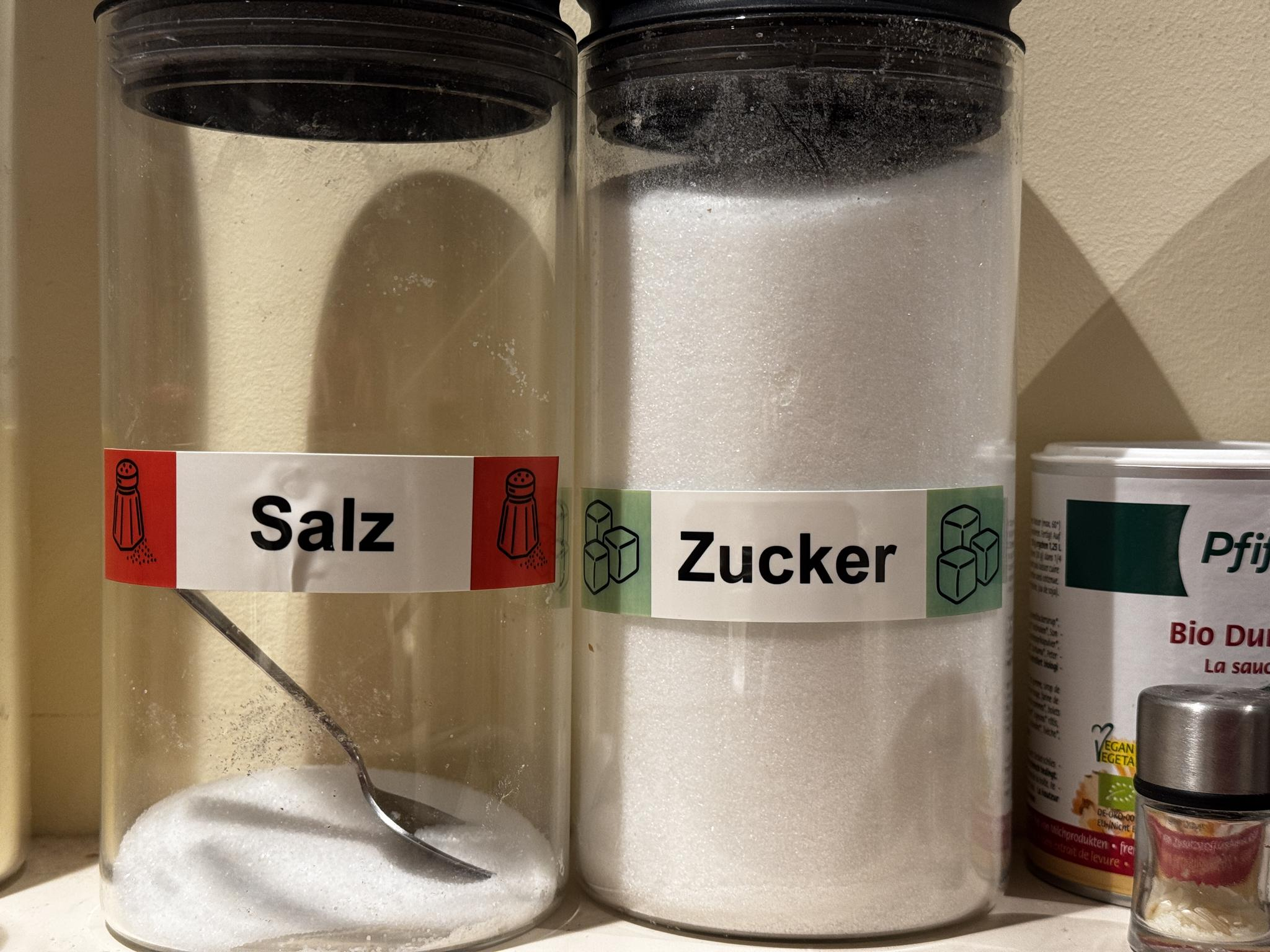 Zwei Vorratsdosen für Salz und Zucker die mit großen farbigen Etiketten gekennzeichnet sind