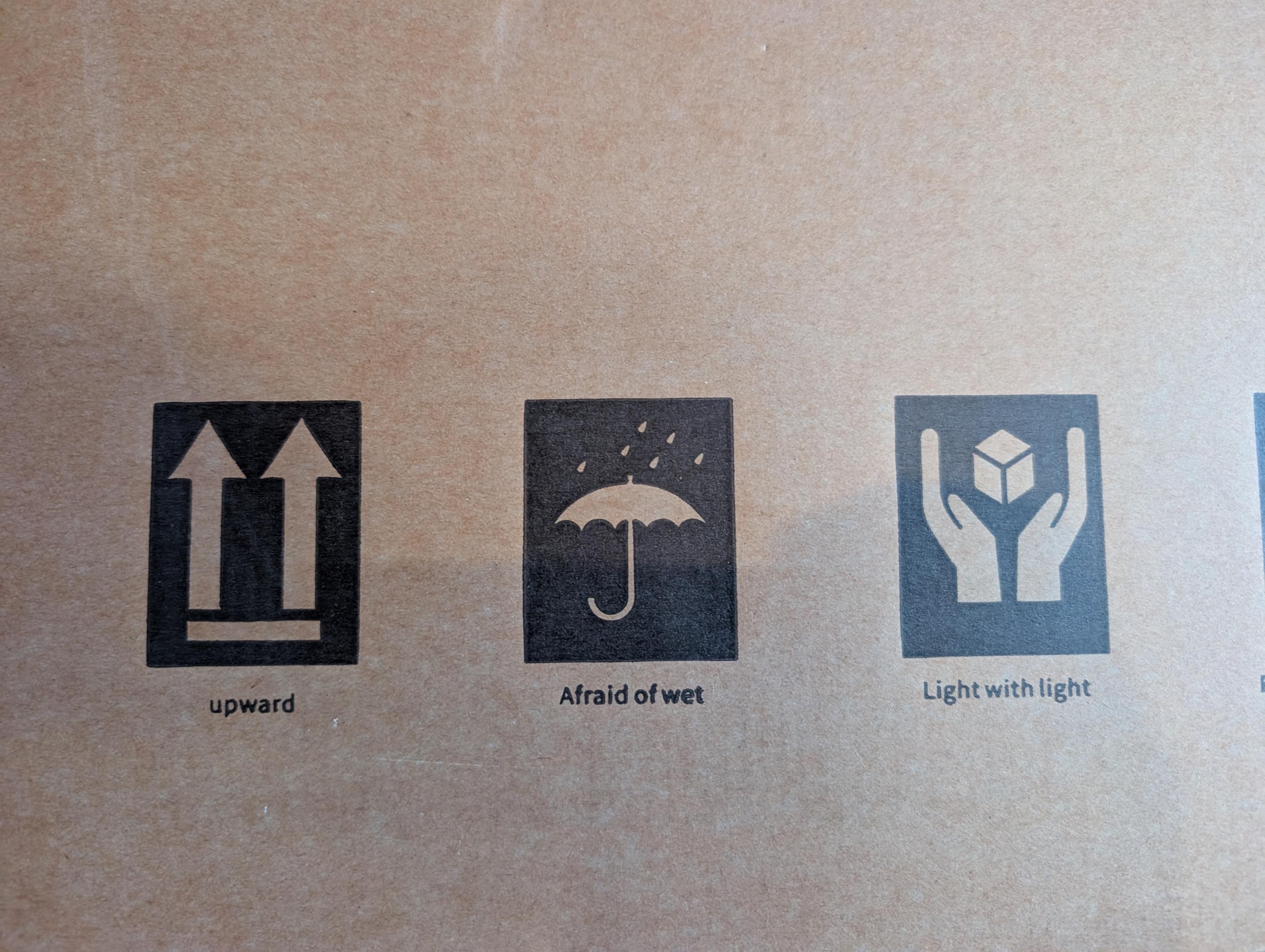 Three shipping symbols with unconventional labels. "this side up" is labeled "upward". "keep dry" is labeled "Afraid of wet". And, "handle with care" is labeled "Light with light".